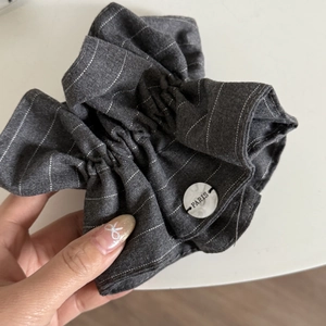 Close-up of dark grey striped scrunchie with pleated texture and white Paris button