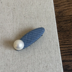 Detail view of denim blue fabric hair clip with a vintage white pearl on linen fabric