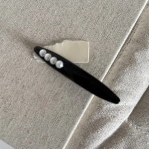 Détail d'une pince à cheveux noire avec quatre perles blanches sur fond de toile