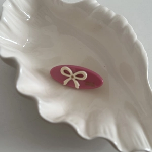 Pink oval acetate hair clip featuring a white bow design on a leaf ceramic tray