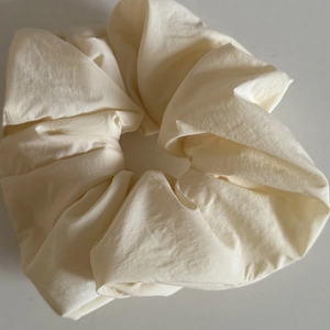 Close-up of a large cream-colored matte fabric scrunchie with soft pleated texture details