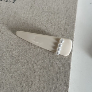 Gros plan d'une pince à cheveux crème avec quatre perles blanches sur fond de lin