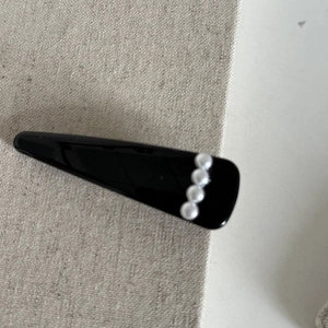 Détail d'une pince à cheveux triangulaire en acrylique noir ornée de perles blanches