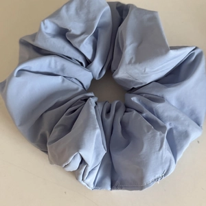 Light blue oversized pleated fabric scrunchie with detailed stitching on white background