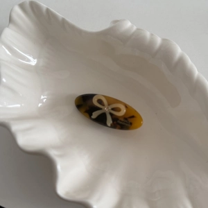 Detailed macro view of tortoiseshell acetate hair clip with white bow and gold lettering