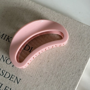 Detailed view of a soft pink glossy hair claw clip on a textured beige canvas book