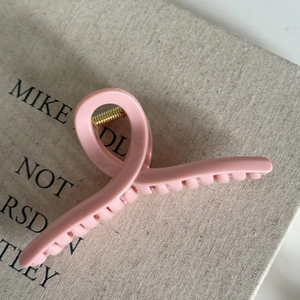 Detail view of the pink twisted claw clip with gold spring on linen texture background