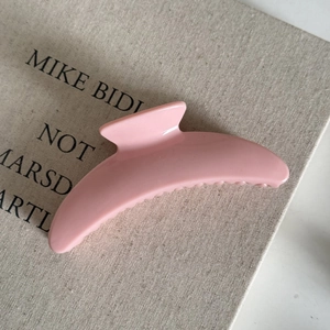 Close-up of a pink crescent hair claw clip on a texture book showing smooth glossy finish