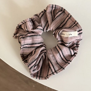 Detail eines rosa-schwarz gestreiften Scrunchies mit weißem smile life Stoffetikett