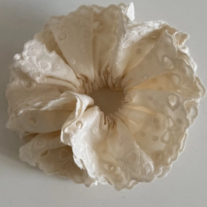 Detail of a cream lace scrunchie with intricate floral eyelet embroidery and wavy edges