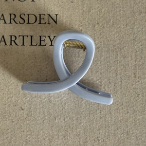 Detailed view of cream blue hair claw clip with golden spring on textured linen fabric