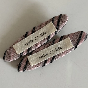 Paar süße Haarspangen aus gestreiftem Stoff mit Smile Life Etiketten im minimalistischen Stil