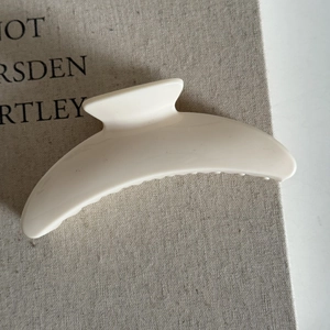 Close-up of a minimalist cream-white curved hair claw clip on a book for daily styling