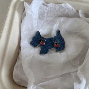 Detail shot of a denim dog-shaped brooch with cherry patterns on a beige tray