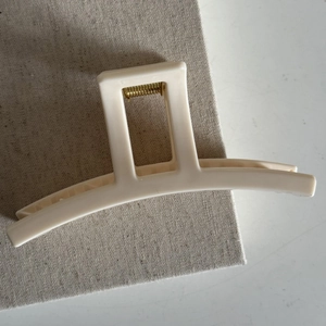 Macro detail of a cream-colored hair claw clip with a sleek rectangular hollow handle