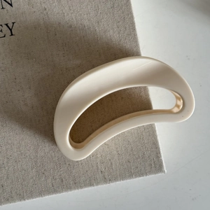 Detail of a creamy white crescent hair claw clip with a glossy finish on textured linen