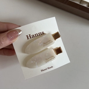 Detail of pearlescent white acetate hair clips with golden metal base on a display card