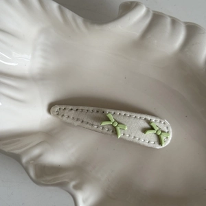 Detail of sweet beige fabric hair clip with small light green bows on a white tray