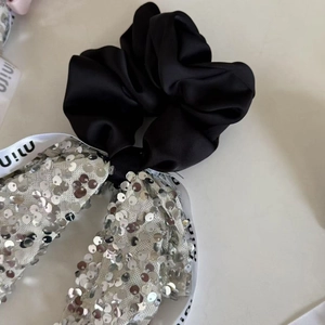 Elegant black satin hair scrunchie with silver sequin bow and white logo ribbon detail