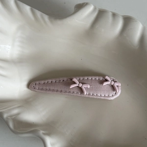 Close-up of pink fabric-wrapped hair clip with sweet 3D bow accents on a ceramic tray