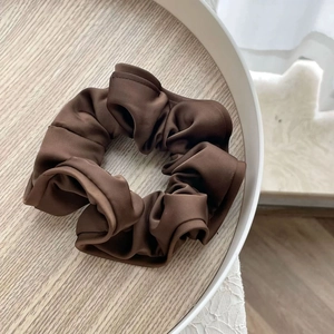Vue détaillée d'un chouchou en satin marron avec texture brillante sur plateau blanc