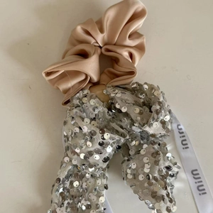 Detail of champagne satin scrunchie featuring silver sequin bow and logo ribbon