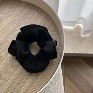 Gros plan d'un chouchou en tissu plissé noir sur un plateau en bois et ombres douces