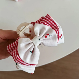 Dettaglio del ricamo a ciliegia e motivo gingham rosso su un fermaglio a fiocco dolce