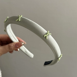 Close-up of wide sage green satin headband with five 3D bow ornaments and soft silk texture