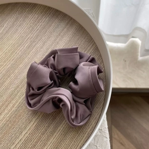Détail d'un chouchou en satin violet poudré élégant avec texture soyeuse sur plateau bois