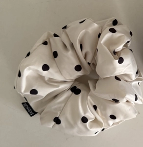 Dettaglio di un elastico per capelli a pois bianco crema con etichetta nera e pizzo