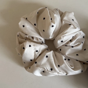 Dettaglio macro dello scrunchie in raso crema con cuori neri e bordi in pizzo eleganti