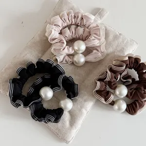 Détail de trois chouchous en dentelle rose, noir et marron ornés de grandes perles blanches
