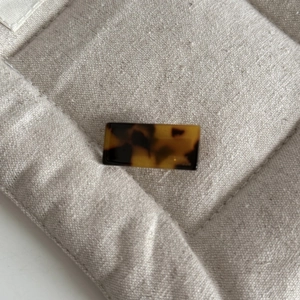 Macro view of rectangular tortoiseshell hair clip with gold label on beige linen