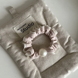 Détail d'un chouchou en dentelle rose avec perle posé sur un sac en coton matelassé