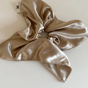 Détail d'un chouchou en satin doré champagne avec effet brillant et étiquette logo