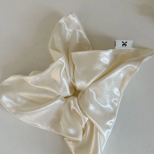 Détail d'un chouchou en satin blanc crème avec texture lisse et étiquette logo