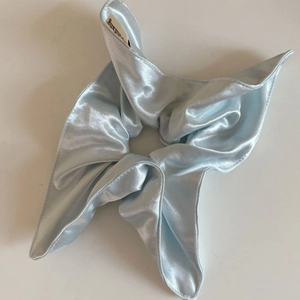 Détail du chouchou en satin bleu clair brillant avec de larges ailes sur fond blanc