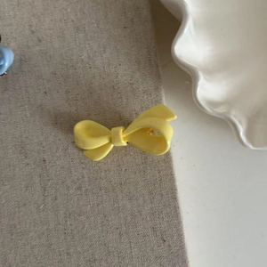 Vibrant yellow bow hair clip with matte texture on a minimalist ceramic display