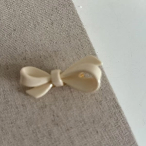 Elegant cream white acrylic bow hair clip for girls placed on a textured fabric background