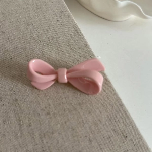 Close-up of a pink acrylic bow hair clip on a minimalist textured fabric background