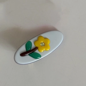Nahaufnahme einer ovalen Haarspange mit gelber Blume und glitzerndem Strassstein