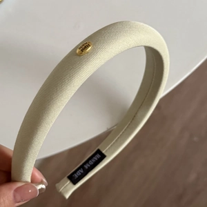 Détail du serre-tête beige en tissu avec étiquette en métal doré et texture en sergé épais