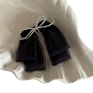 Elegant black ribbon hair clip with beaded silver bow detail on a white ceramic shell plate