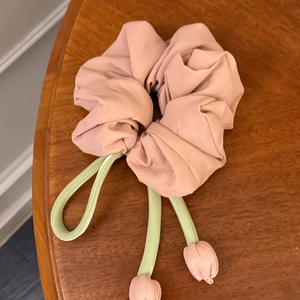 Détail d'un chouchou tulipe rose avec longs rubans verts sur une table en bois