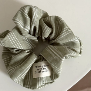 Détail du chouchou rayé vert sauge avec étiquette slogan et texture du tissu
