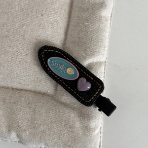 Denim bow hair clip with a smile badge and purple heart on a soft quilted background