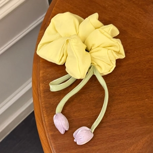 Détail d'un chouchou jaune en tissu avec breloques tulipes mauves sur une table en bois