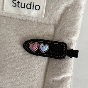 Close-up of black denim hair clip with yellow stitching and heart resin buttons