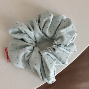 Macro detail of light blue fabric scrunchie featuring grey star pattern and pink label